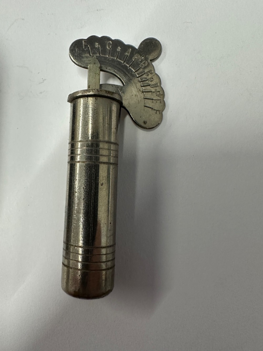A cylindrical nickel-plated chromatic variable pitch pipe with a note scale arc sitting inside its open red metal case. View X