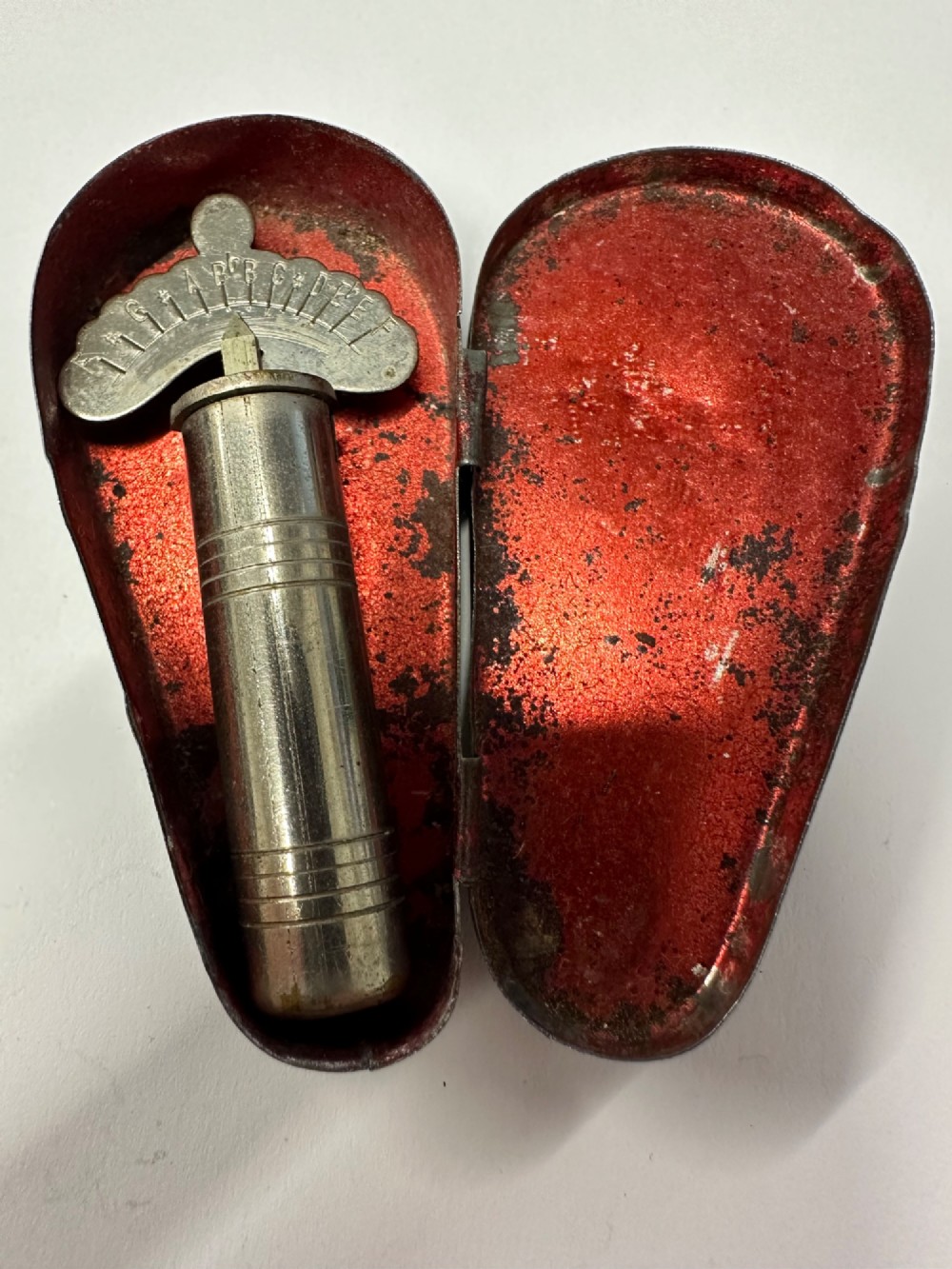 A cylindrical nickel-plated chromatic variable pitch pipe with a note scale arc sitting inside its open red metal case.