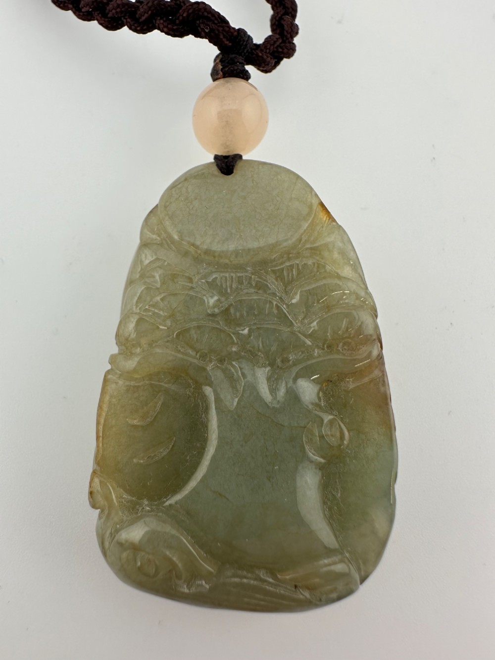 A hand-carved yellow and green jade pendant depicting a phoenix among foliage, suspended from a cord with a spherical accent bead. View II