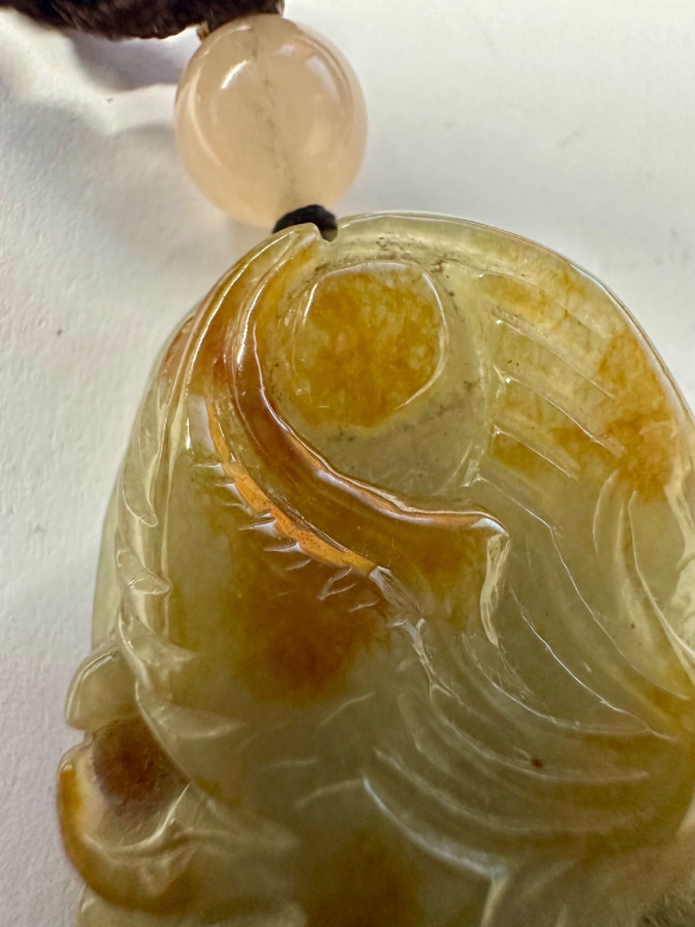 A hand-carved yellow and green jade pendant depicting a phoenix among foliage, suspended from a cord with a spherical accent bead. View III