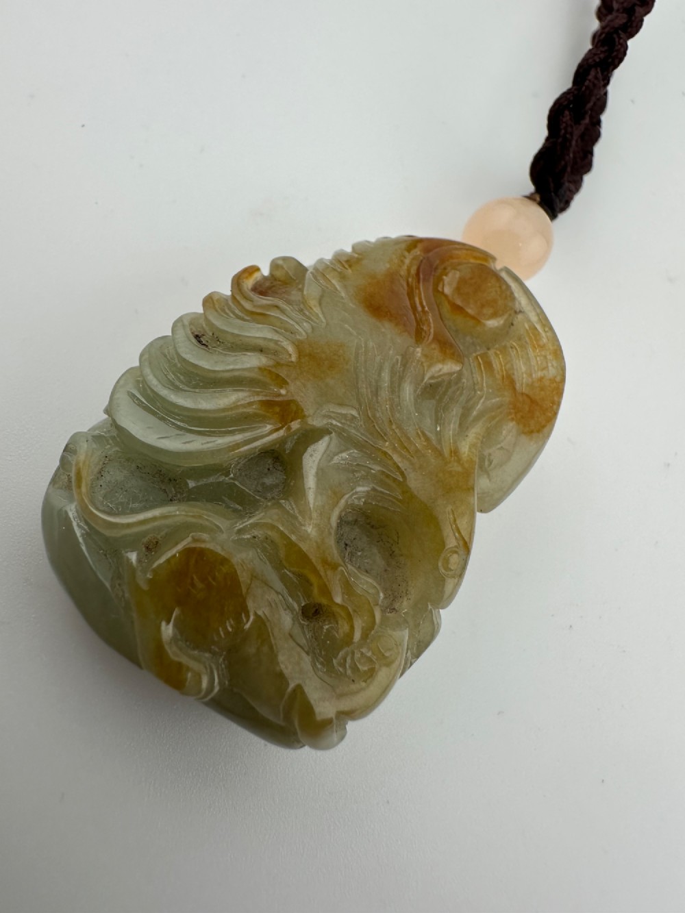 A hand-carved yellow and green jade pendant depicting a phoenix among foliage, suspended from a cord with a spherical accent bead. View V