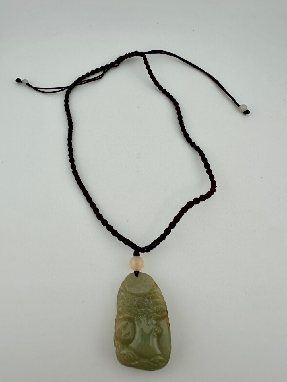 A hand-carved yellow and green jade pendant depicting a phoenix among foliage, suspended from a cord with a spherical accent bead. View VII