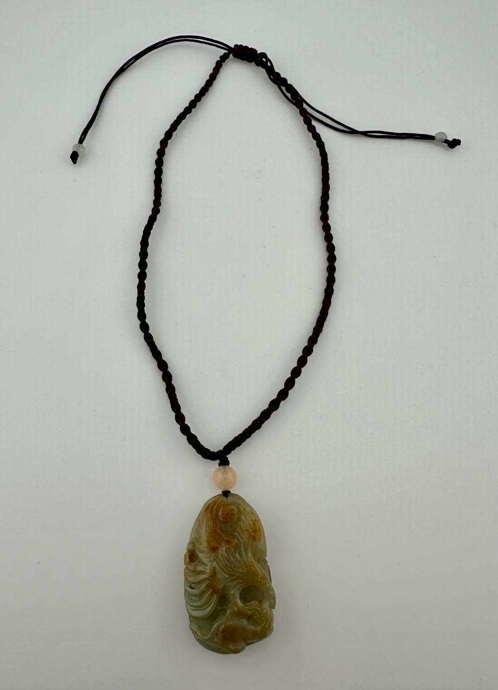 A hand-carved yellow and green jade pendant depicting a phoenix among foliage, suspended from a cord with a spherical accent bead. View VIII