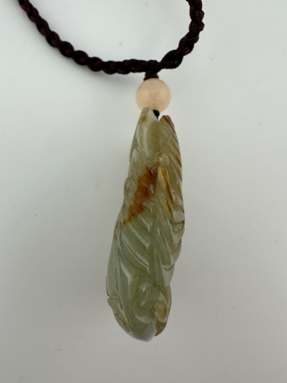 A hand-carved yellow and green jade pendant depicting a phoenix among foliage, suspended from a cord with a spherical accent bead. View IX