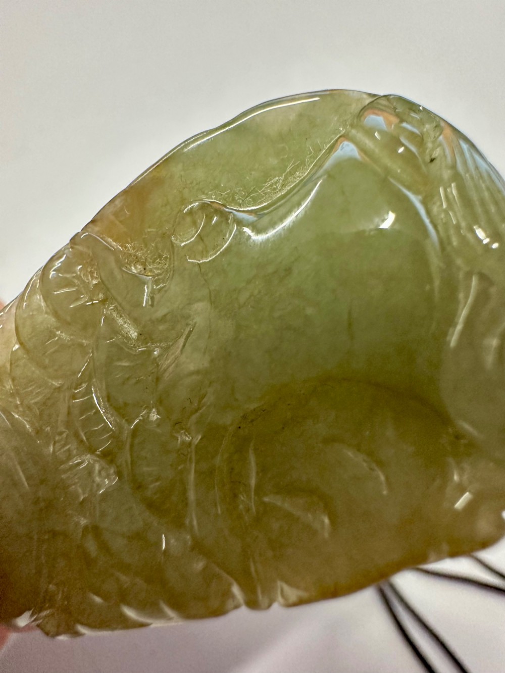 A hand-carved yellow and green jade pendant depicting a phoenix among foliage, suspended from a cord with a spherical accent bead. View XI