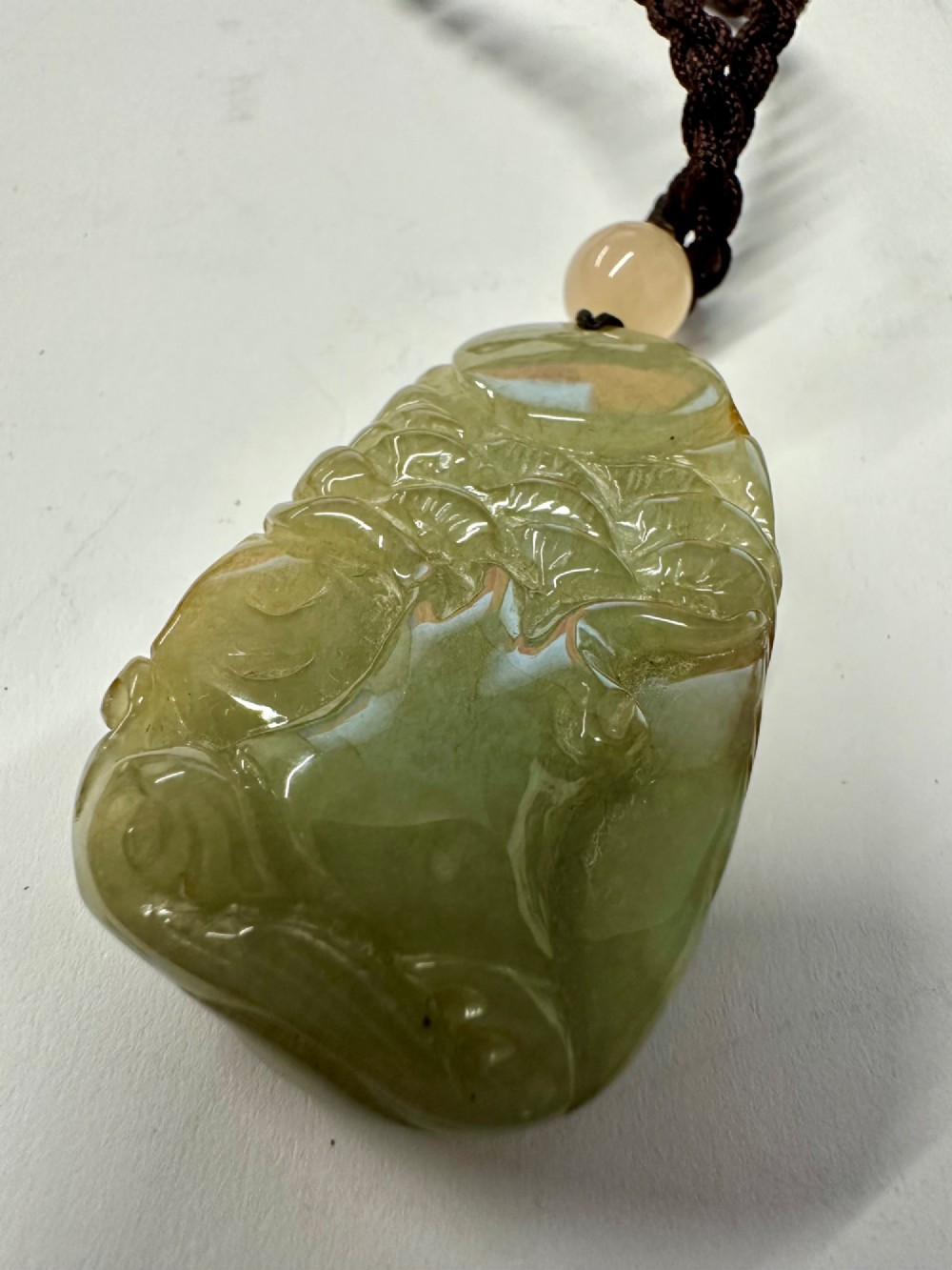 A hand-carved yellow and green jade pendant depicting a phoenix among foliage, suspended from a cord with a spherical accent bead. View XII