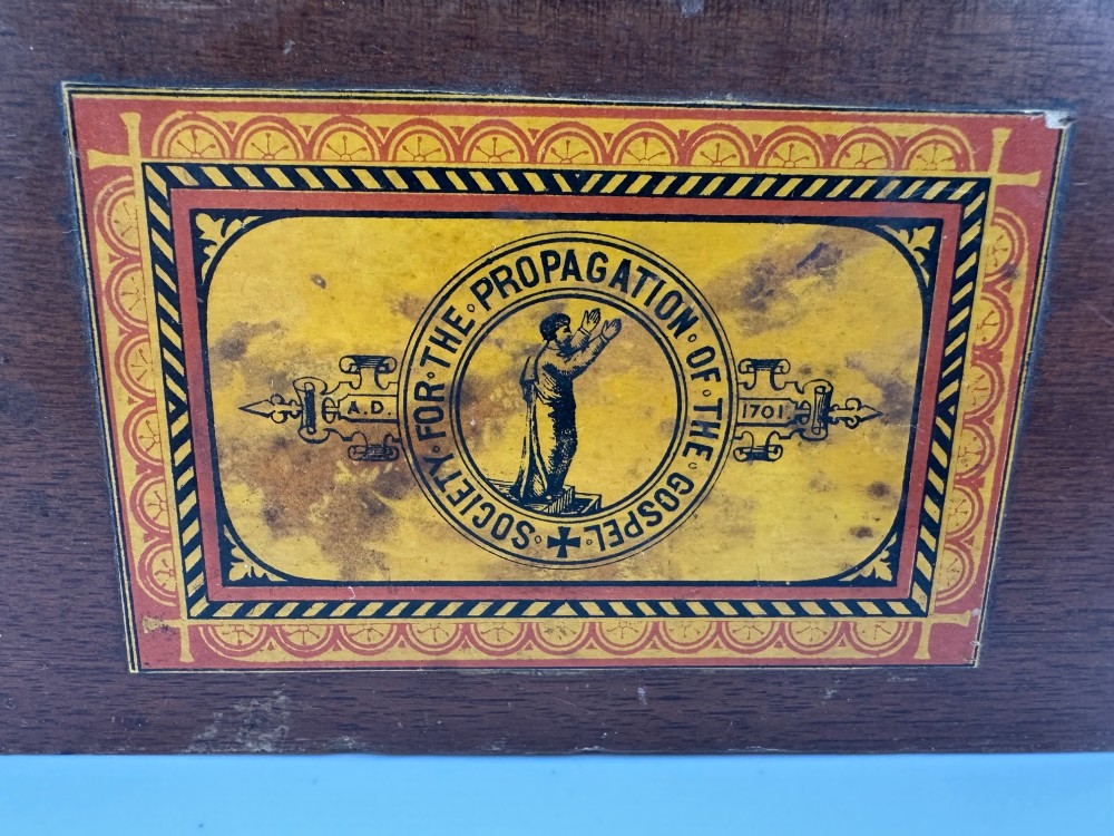 A rectangular dark wooden church collection box featuring a coin slot on top and a printed yellow and red Society for the Propagation of the Gospel label on the front. View III