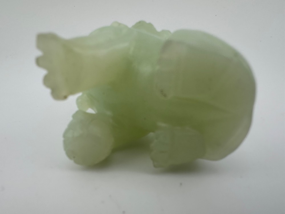 A hand-carved pale green jade guardian lion sculpture resting on a dark carved timber base. View VIII