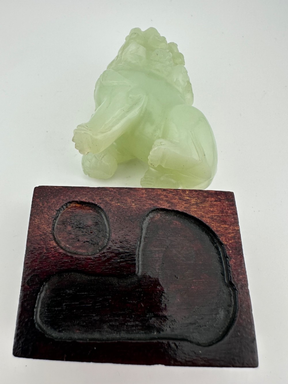 A hand-carved pale green jade guardian lion sculpture resting on a dark carved timber base. View IX
