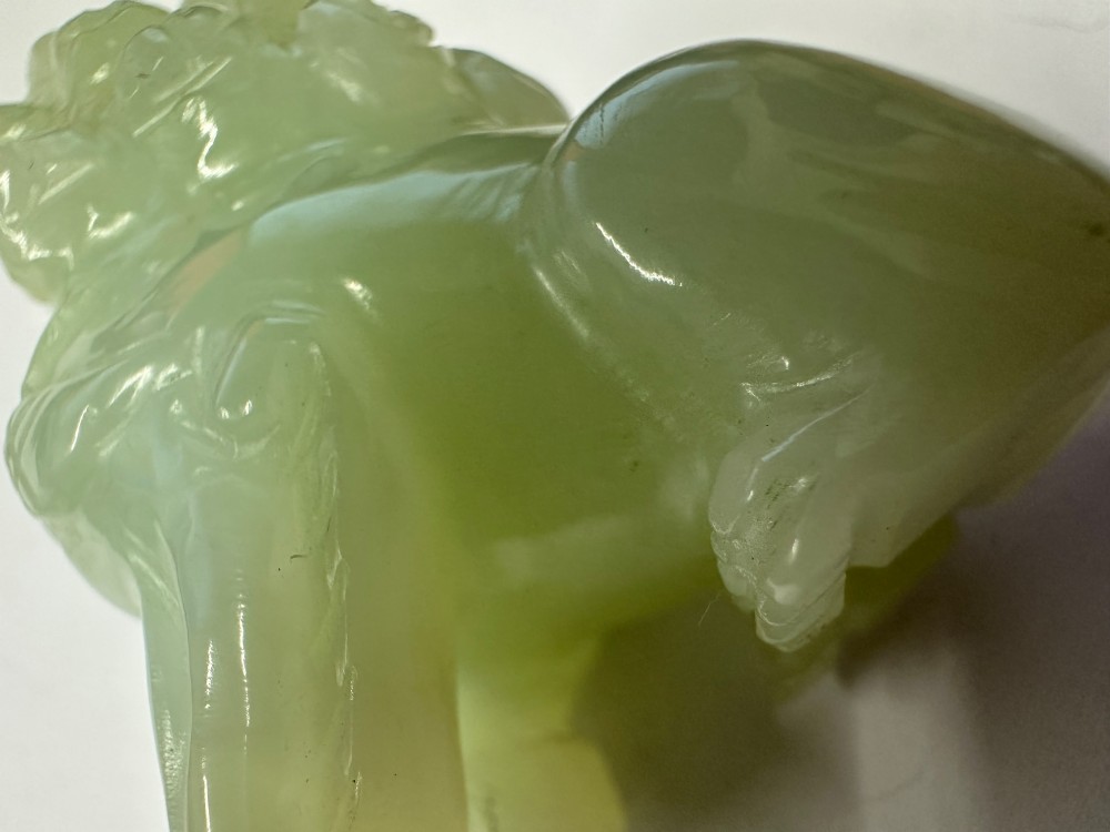 A hand-carved pale green jade guardian lion sculpture resting on a dark carved timber base. View XII
