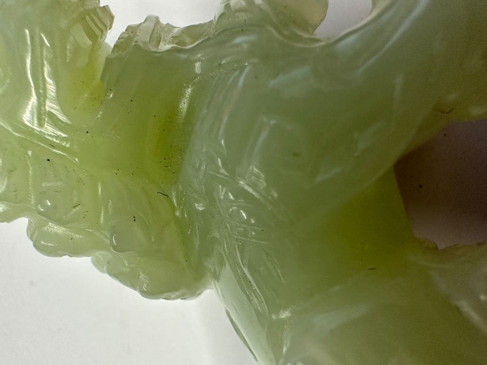 A hand-carved pale green jade guardian lion sculpture resting on a dark carved timber base. View XIII