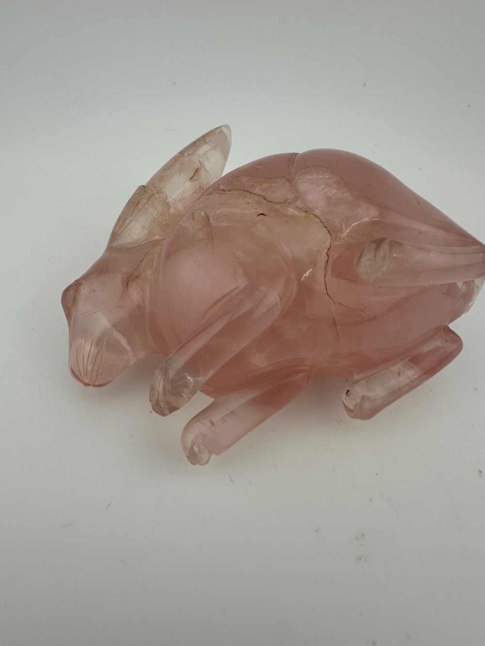 A hand-carved pink rose quartz rabbit figurine with upright ears seated on a dark fitted hardwood display base. View V