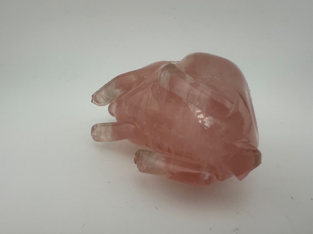 A hand-carved pink rose quartz rabbit figurine with upright ears seated on a dark fitted hardwood display base. View VII