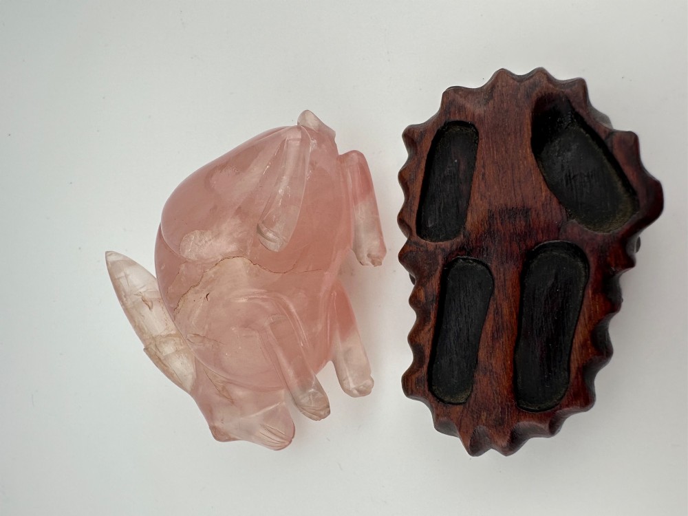 A hand-carved pink rose quartz rabbit figurine with upright ears seated on a dark fitted hardwood display base. View X