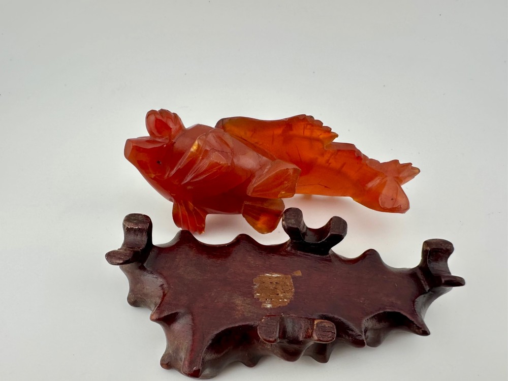 A translucent terracotta orange carnelian agate sculpture of a fantail goldfish positioned on a carved dark brown hardwood stand. View VIII