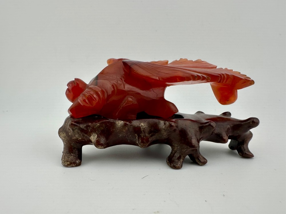 A translucent terracotta orange carnelian agate sculpture of a fantail goldfish positioned on a carved dark brown hardwood stand. View X