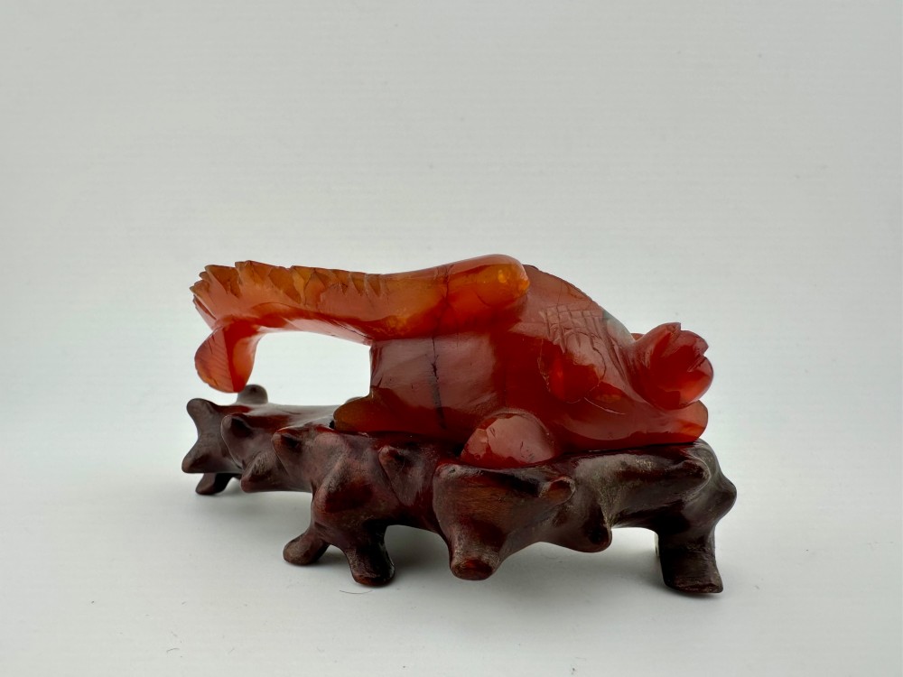 A translucent terracotta orange carnelian agate sculpture of a fantail goldfish positioned on a carved dark brown hardwood stand. View XI