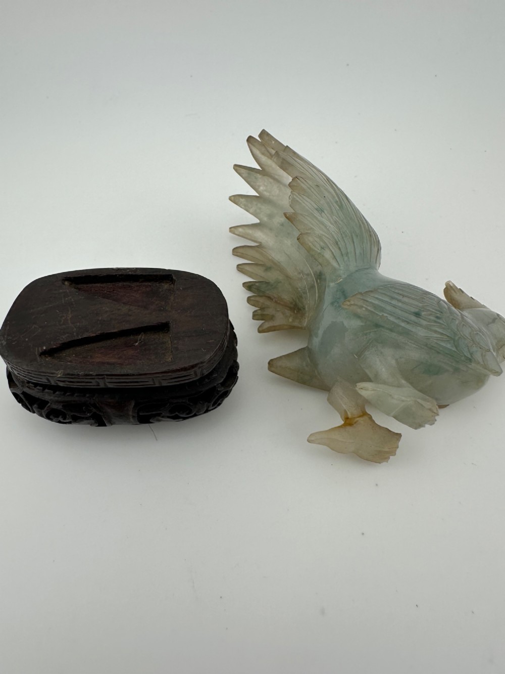 A hand-carved pale green jade sculpture of a cockerel with fan-shaped tail feathers, displayed on a dark carved hardwood base. View VIII