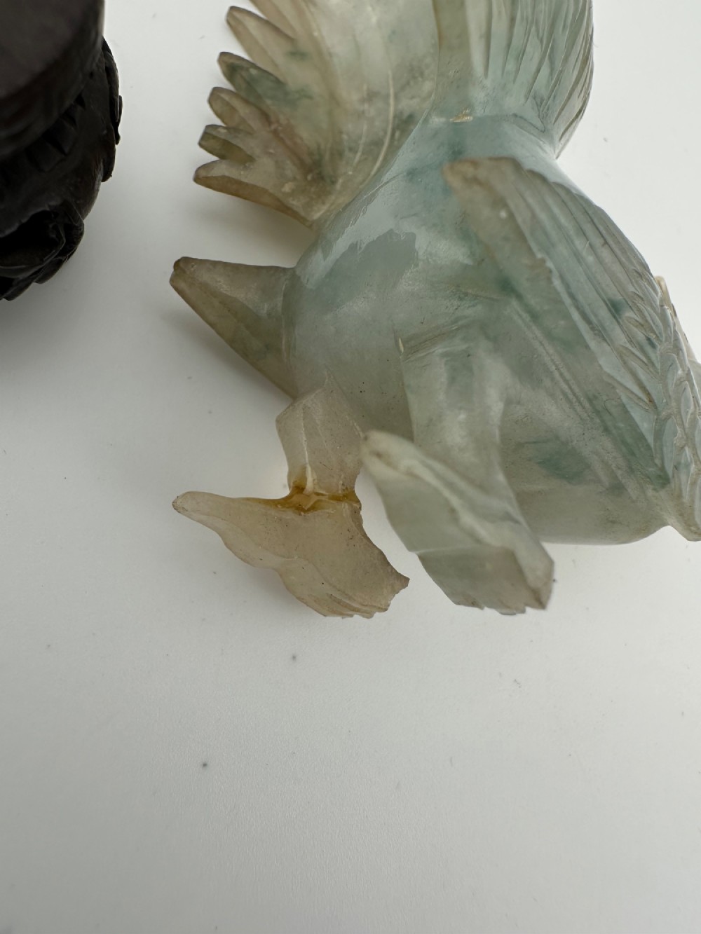 A hand-carved pale green jade sculpture of a cockerel with fan-shaped tail feathers, displayed on a dark carved hardwood base. View IX