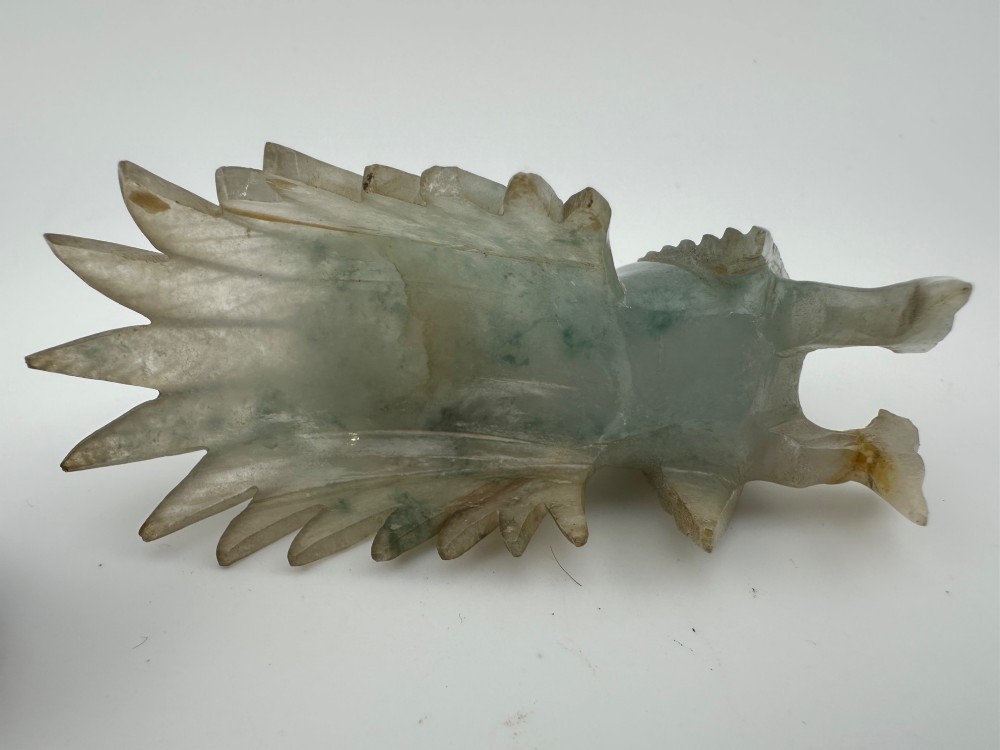 A hand-carved pale green jade sculpture of a cockerel with fan-shaped tail feathers, displayed on a dark carved hardwood base. View X