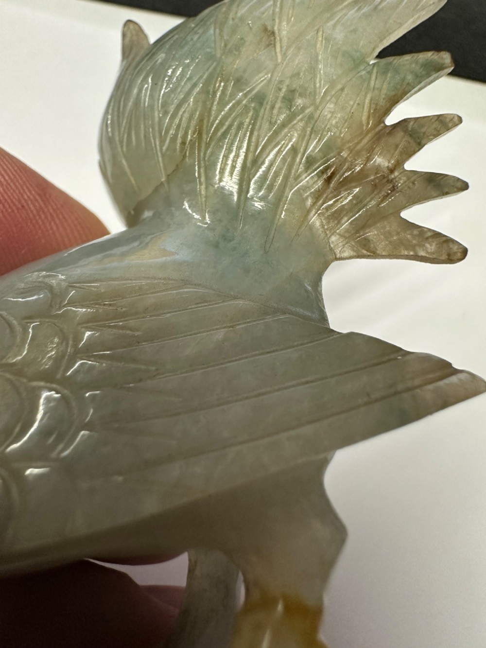 A hand-carved pale green jade sculpture of a cockerel with fan-shaped tail feathers, displayed on a dark carved hardwood base. View XV