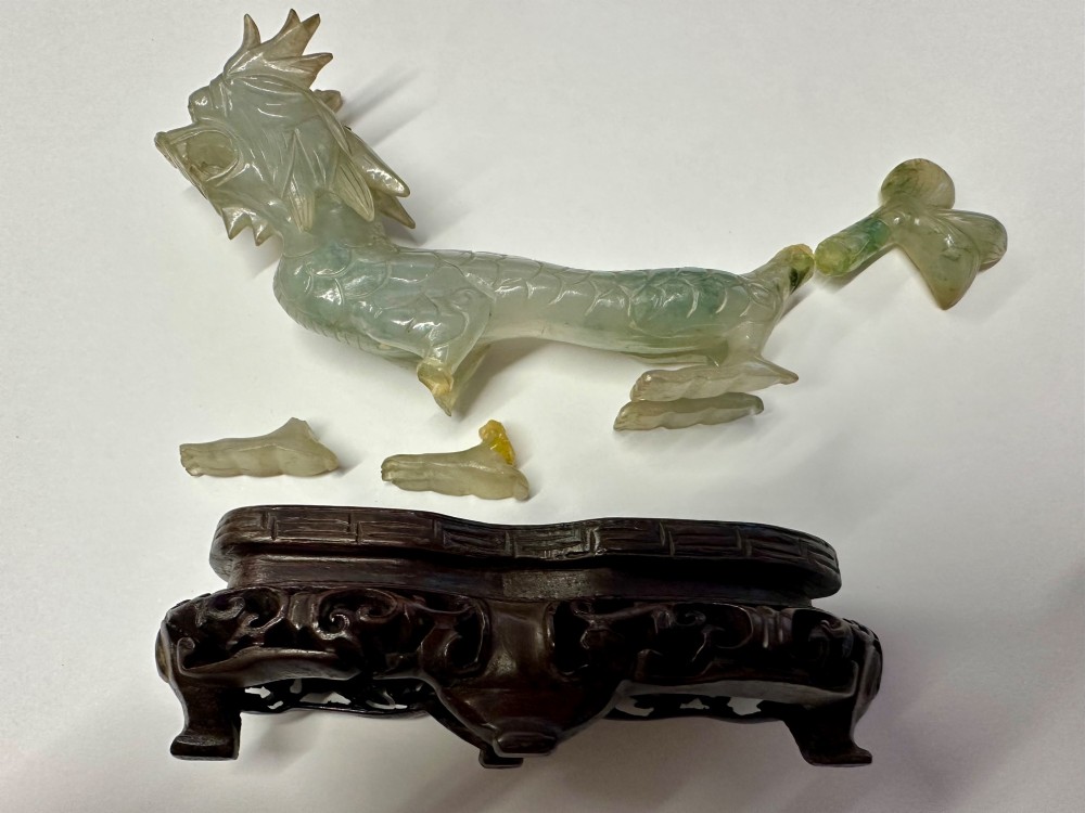 A carved pale green jade dragon sculpture shown alongside a dark pierced hardwood display stand.