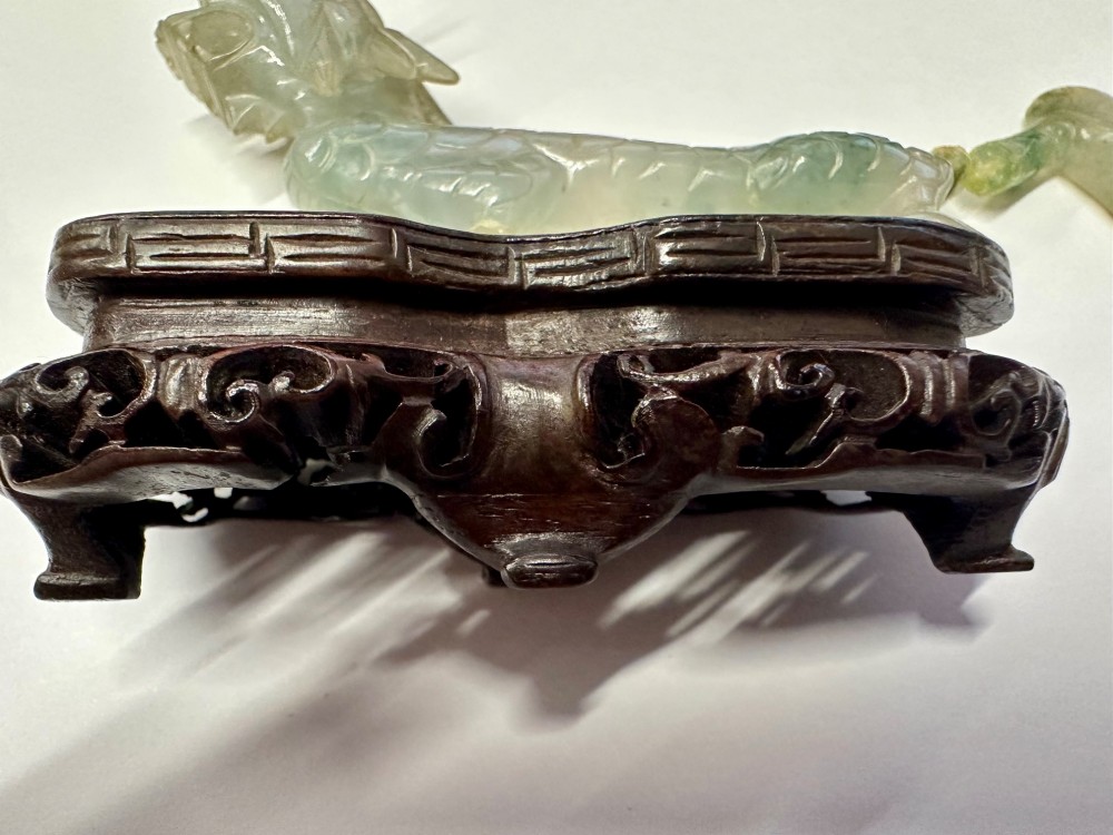 A carved pale green jade dragon sculpture shown alongside a dark pierced hardwood display stand. View II