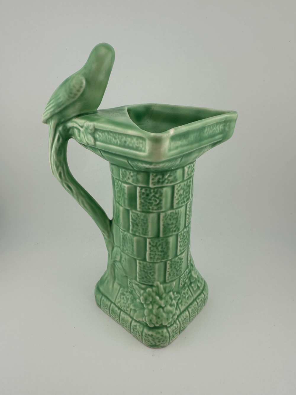 A pale green glazed earthenware Art Deco ceramic jug featuring relief brickwork and a sculpted bird perched on the handle. View III