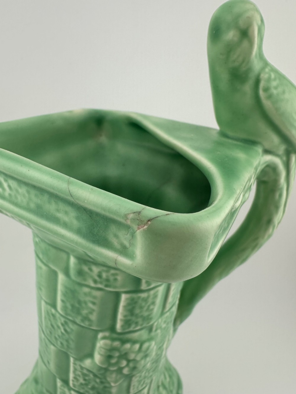 A pale green glazed earthenware Art Deco ceramic jug featuring relief brickwork and a sculpted bird perched on the handle. View VI