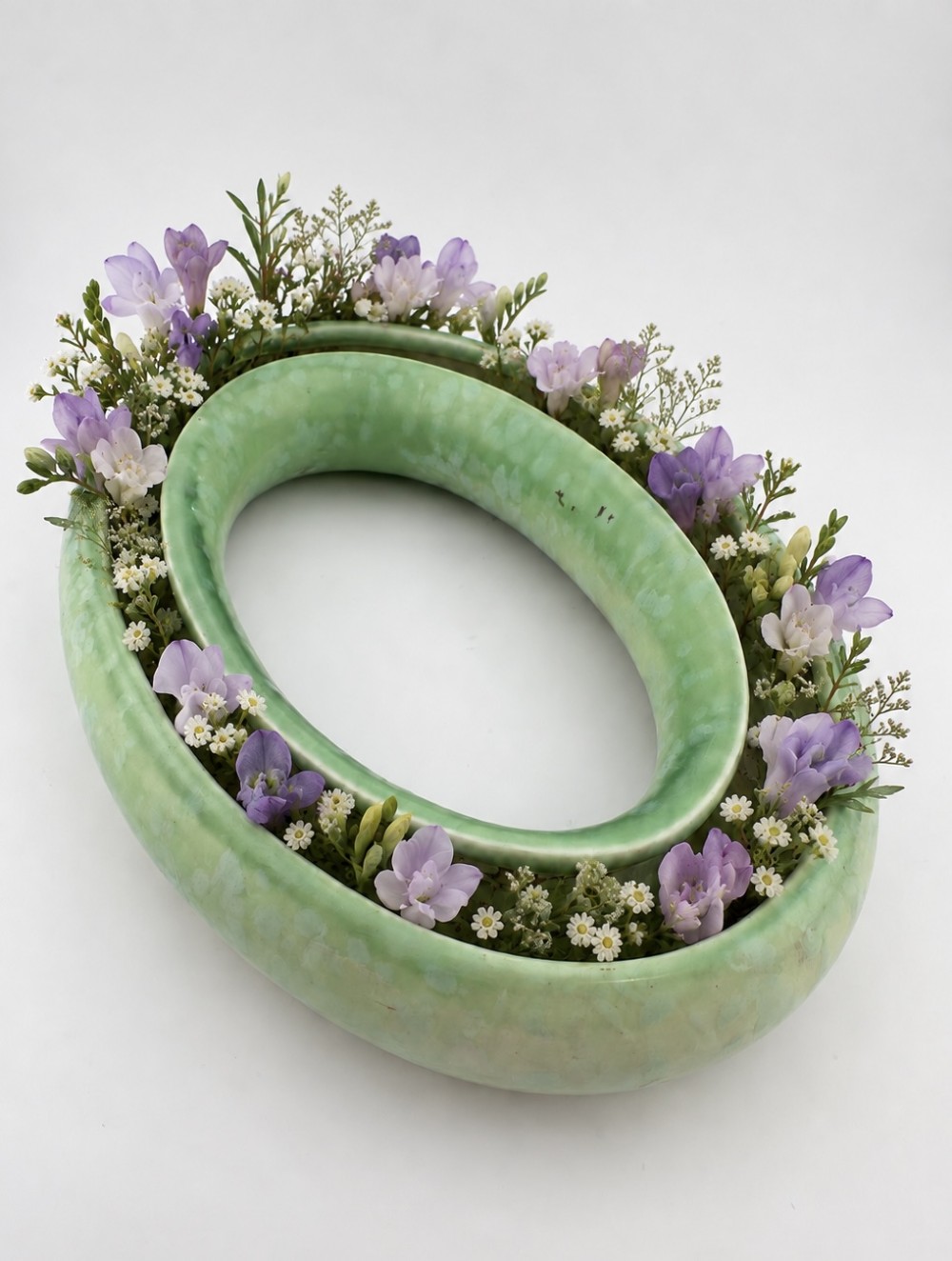 A 1930s oval ceramic posy ring vase with a mottled green glaze, featuring a hollow ring trough designed for short floral stems.