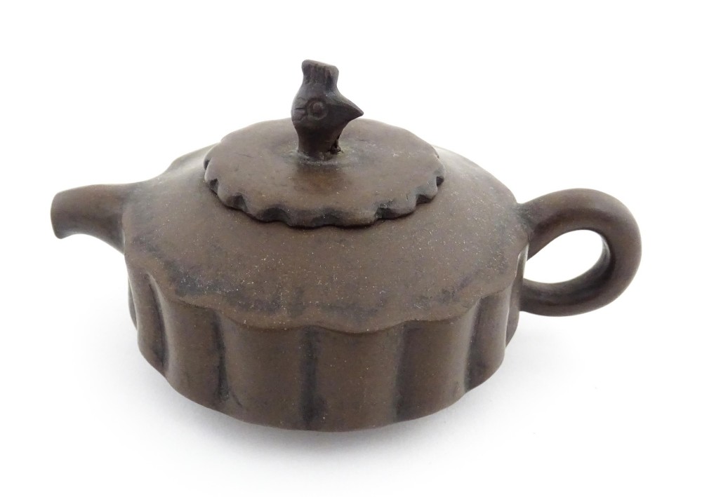 A small dark brown unglazed ceramic teapot featuring a lobed body and a bird-shaped finial on the lid.