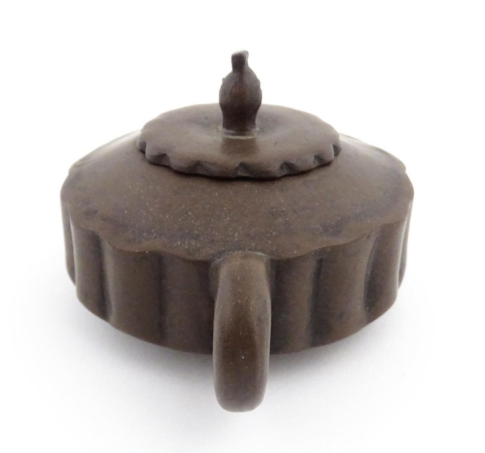 A small dark brown unglazed ceramic teapot featuring a lobed body and a bird-shaped finial on the lid. View VI