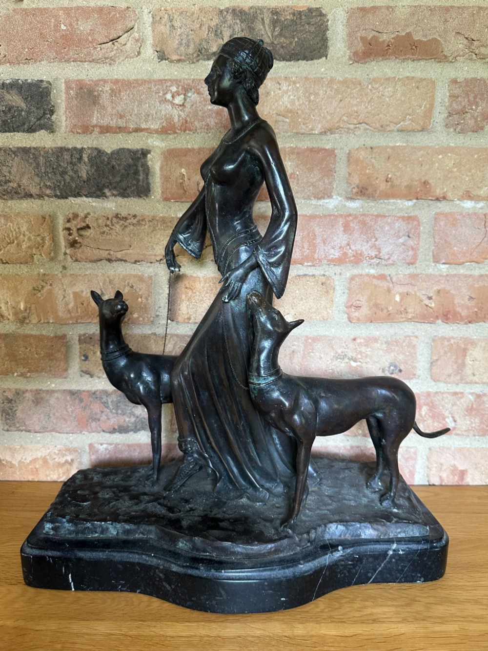 A dark bronze Art Deco sculpture depicting a stylised woman walking two greyhounds on thin chains, set on a dark polished marble base. View V