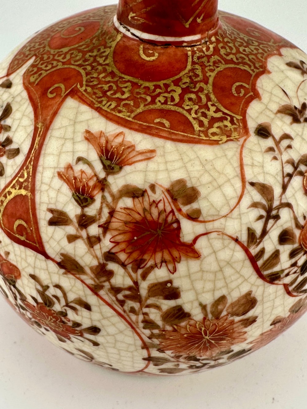 A Japanese Kutani porcelain bottle vase with a tall narrow neck, featuring iron red and gilt floral decoration over a cream crackle glaze body. View X