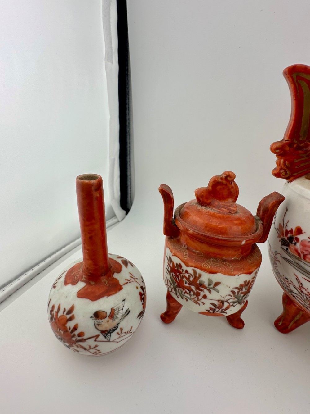 A five-piece Japanese Kutani porcelain garniture set featuring three tripod censers with shishi lion lids and two bottleneck vases in iron-red and polychrome enamel detailing. View V