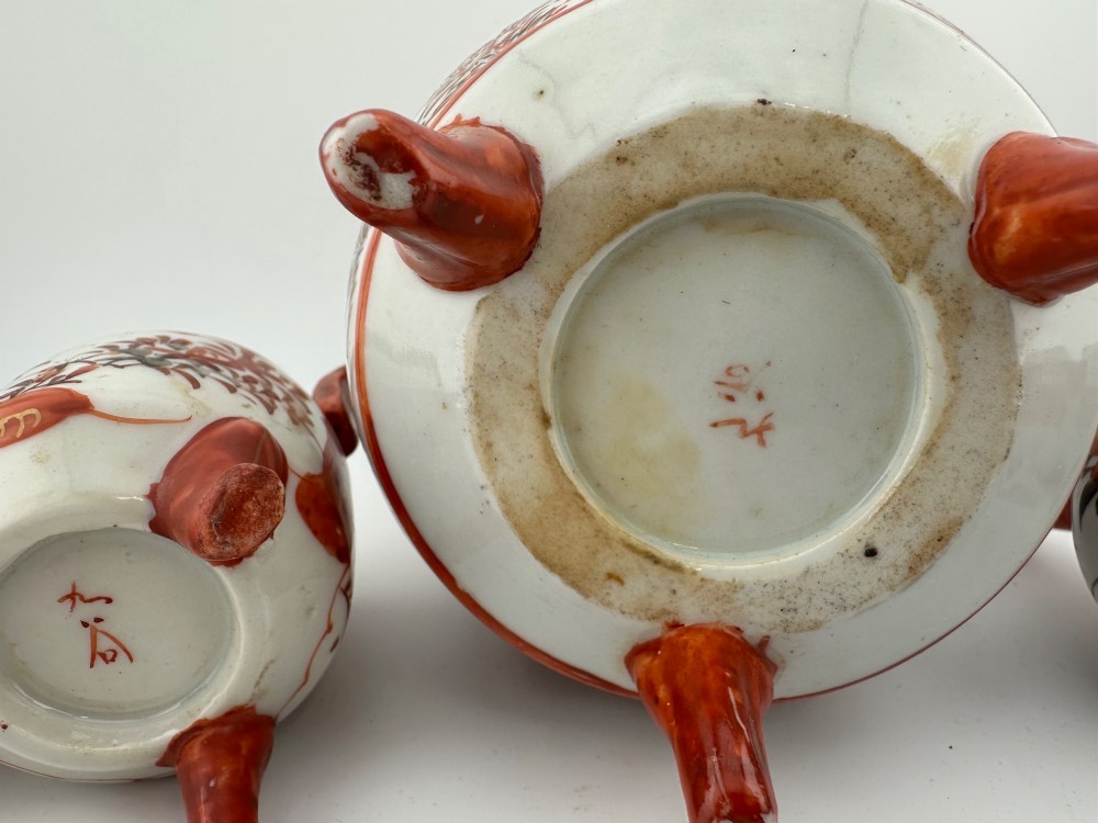 A five-piece Japanese Kutani porcelain garniture set featuring three tripod censers with shishi lion lids and two bottleneck vases in iron-red and polychrome enamel detailing. View IX