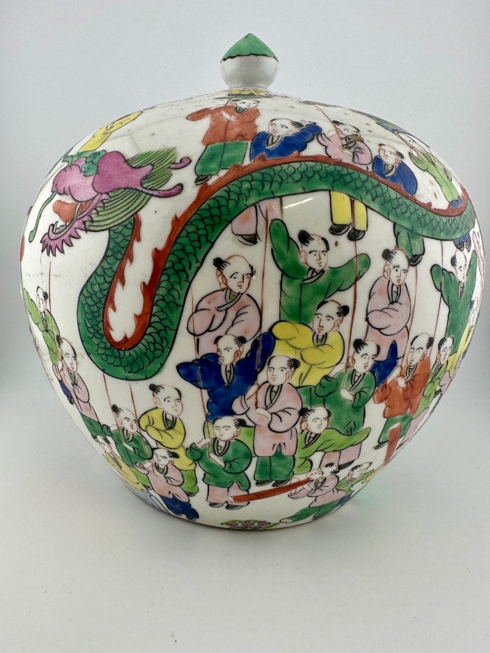 A rounded white porcelain covered jar featuring hand-painted colourful enamels depicting a dragon festival procession with children. View V