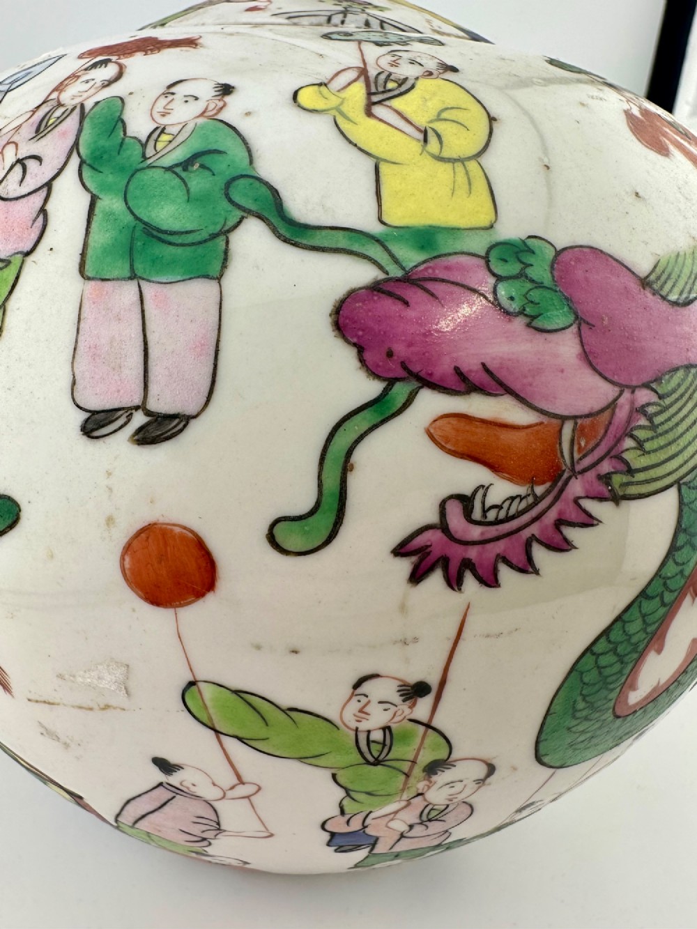 A rounded white porcelain covered jar featuring hand-painted colourful enamels depicting a dragon festival procession with children. View X