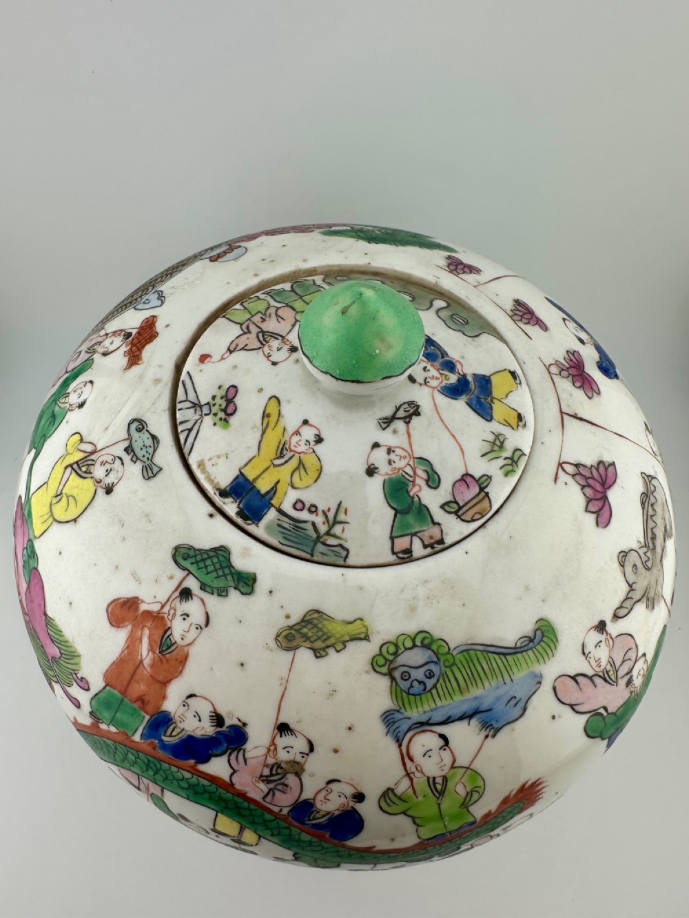 A rounded white porcelain covered jar featuring hand-painted colourful enamels depicting a dragon festival procession with children. View XI