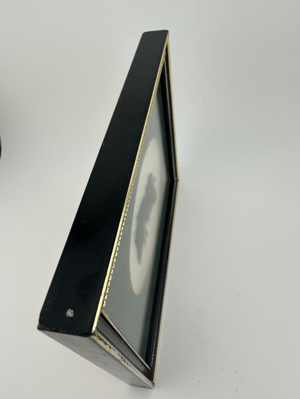 A framed Art Deco silhouette portrait depicting a lady in profile with a decorative hat inside an oval cream mount surrounded by a black and gold frame. View VI