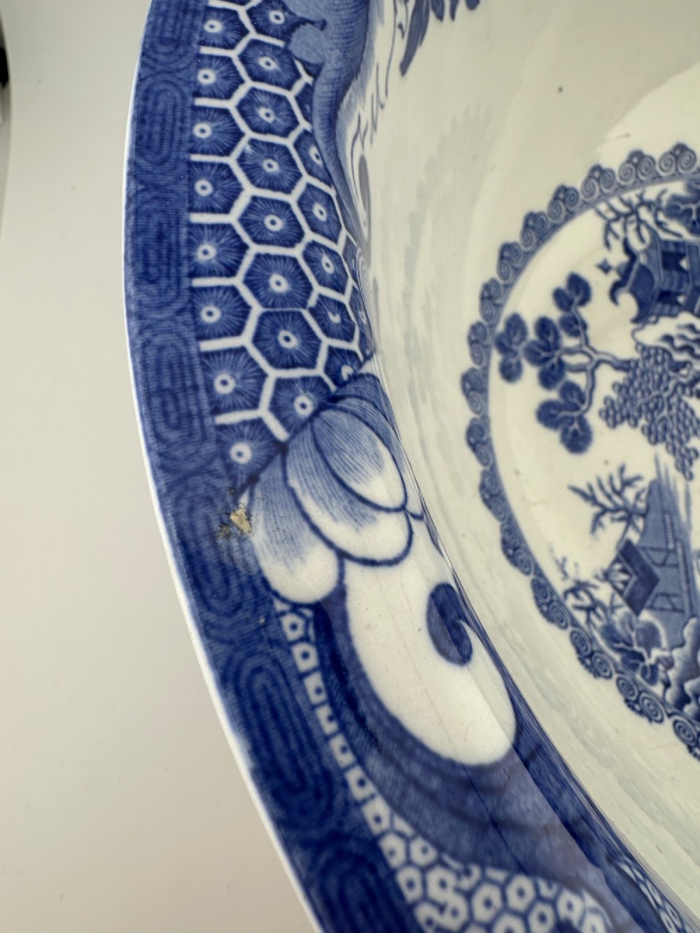 A circular antique blue and white ironstone wash basin bowl featuring a central Chinoiserie landscape scene surrounded by ornate floral and geometric borders. View IX