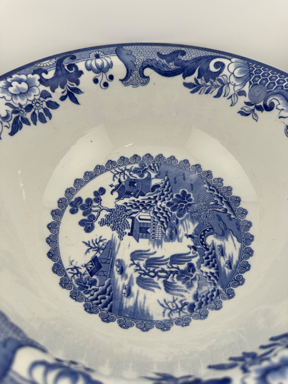 A circular antique blue and white ironstone wash basin bowl featuring a central Chinoiserie landscape scene surrounded by ornate floral and geometric borders. View X