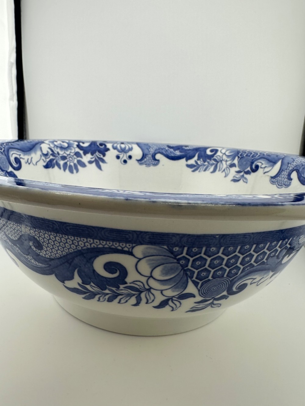 A circular antique blue and white ironstone wash basin bowl featuring a central Chinoiserie landscape scene surrounded by ornate floral and geometric borders. View XI