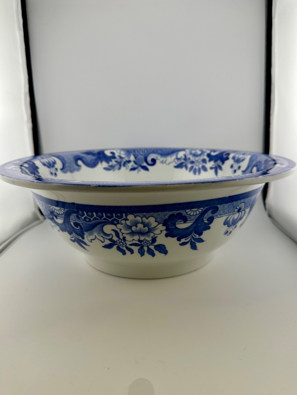 A circular antique blue and white ironstone wash basin bowl featuring a central Chinoiserie landscape scene surrounded by ornate floral and geometric borders. View XII