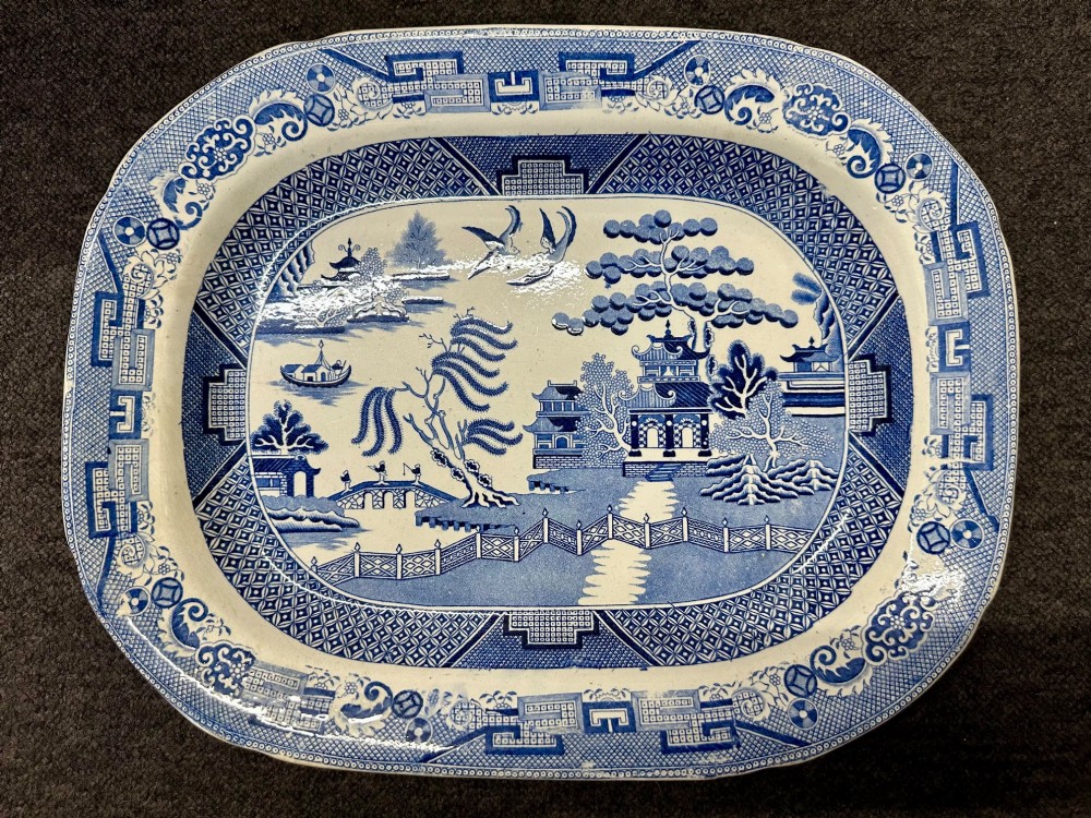 An oval early Victorian Staffordshire earthenware meat platter featuring a cobalt blue and white transferware Willow pattern with pagodas, birds, and a decorative geometric border.