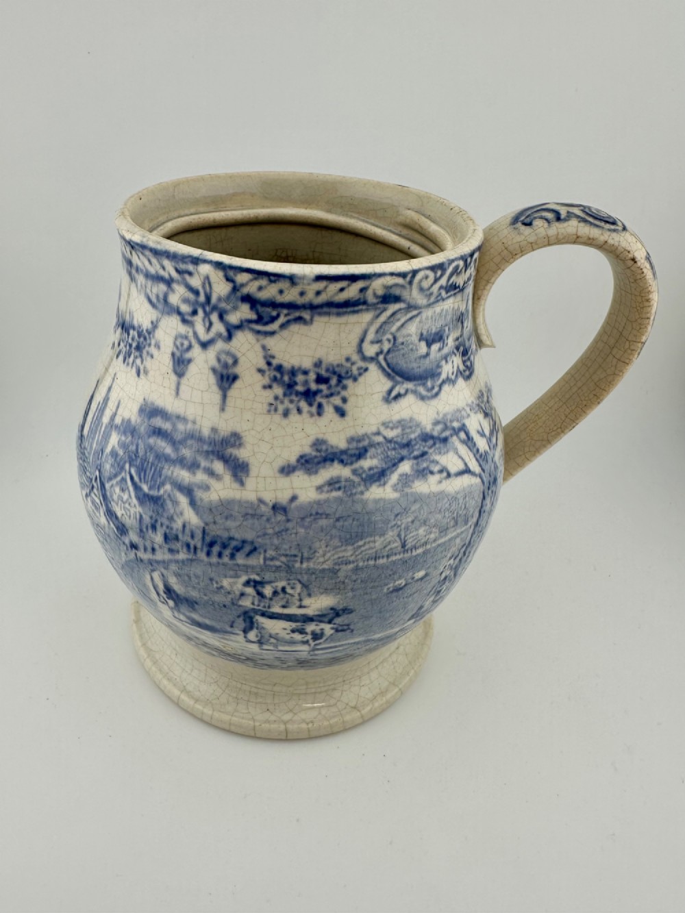 An early Victorian blue and white transferware ceramic jug featuring a pastoral cattle scene with fine glaze crazing throughout.