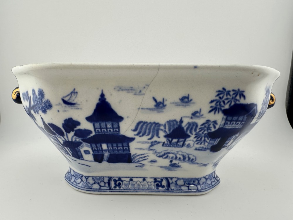 An antique oval ironstone jardiniere featuring blue and white transfer-printed Chinoiserie landscape decoration and small side handles with gilded detailing.