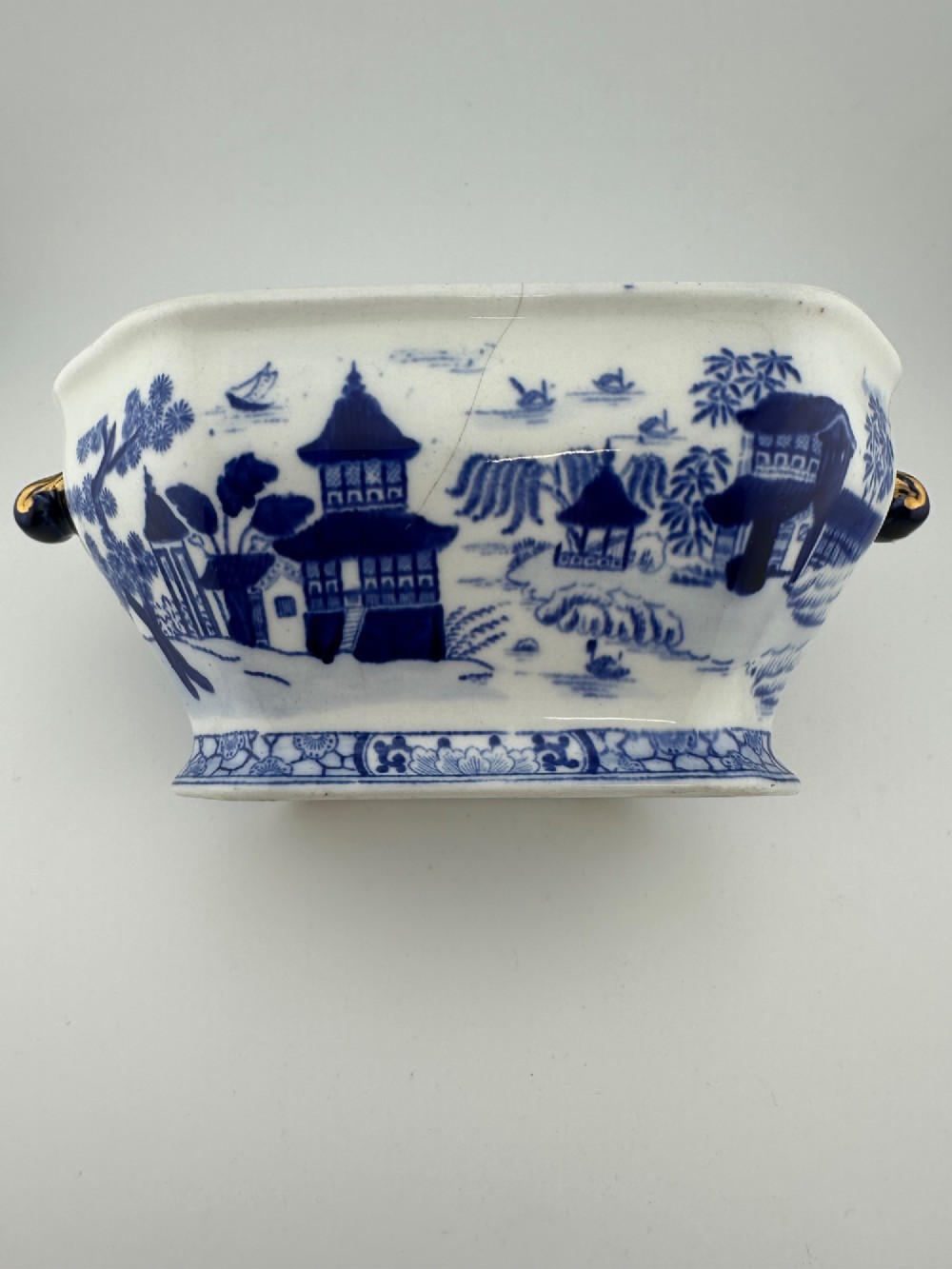 An antique oval ironstone jardiniere featuring blue and white transfer-printed Chinoiserie landscape decoration and small side handles with gilded detailing. View II