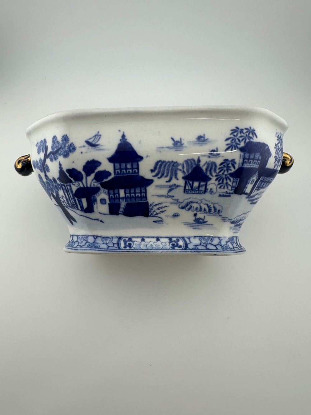 An antique oval ironstone jardiniere featuring blue and white transfer-printed Chinoiserie landscape decoration and small side handles with gilded detailing. View V