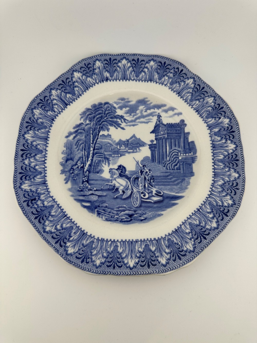An octagonal-edged blue and white transferware plate featuring a central classical chariot scene surrounded by an ornate feather-patterned border.